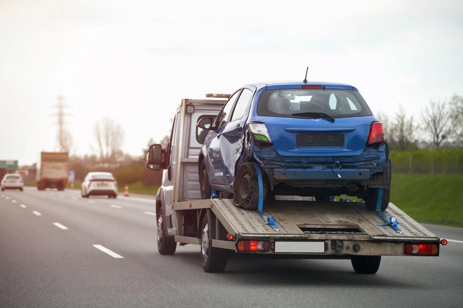 Flatbed tow truck hauling a damaged car on the highway